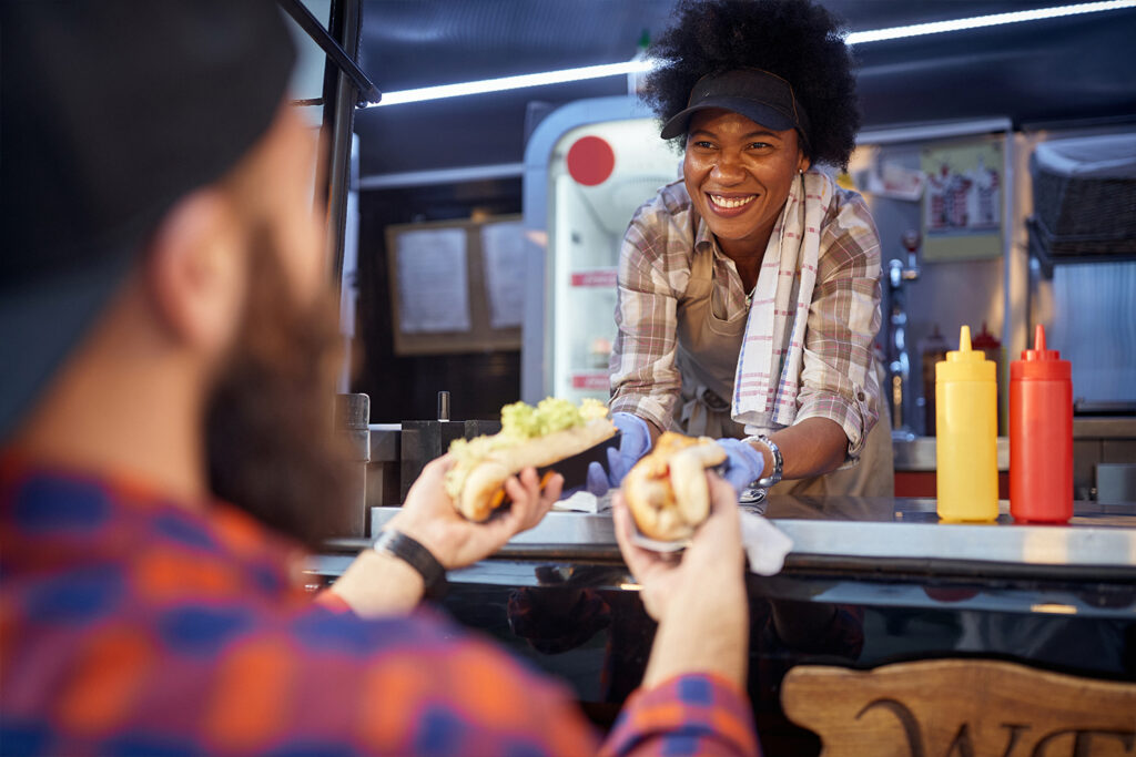 Woman handing a man two hot dogs out the window of a food truck