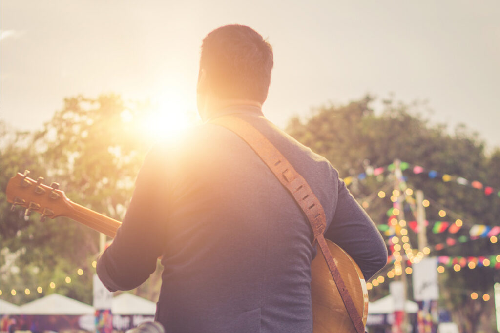 back of man playing guitar at festival as sunsets