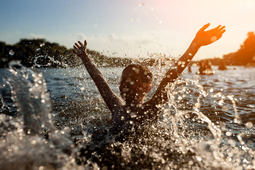 Boy swimming in lake splashing water in front of the camera